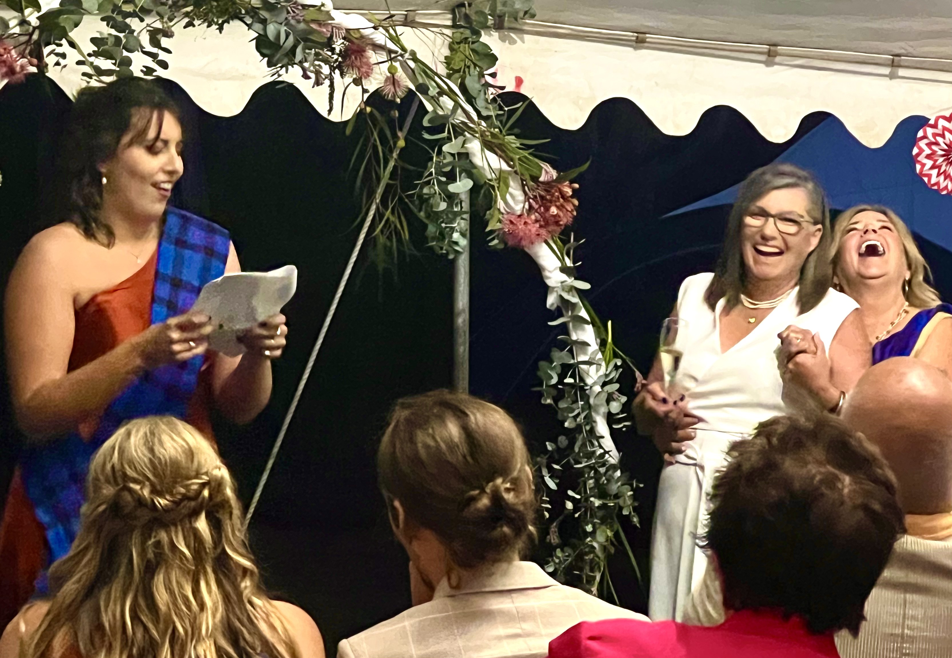 Helen and Penny laughing together during a wedding speech beneath the marquee