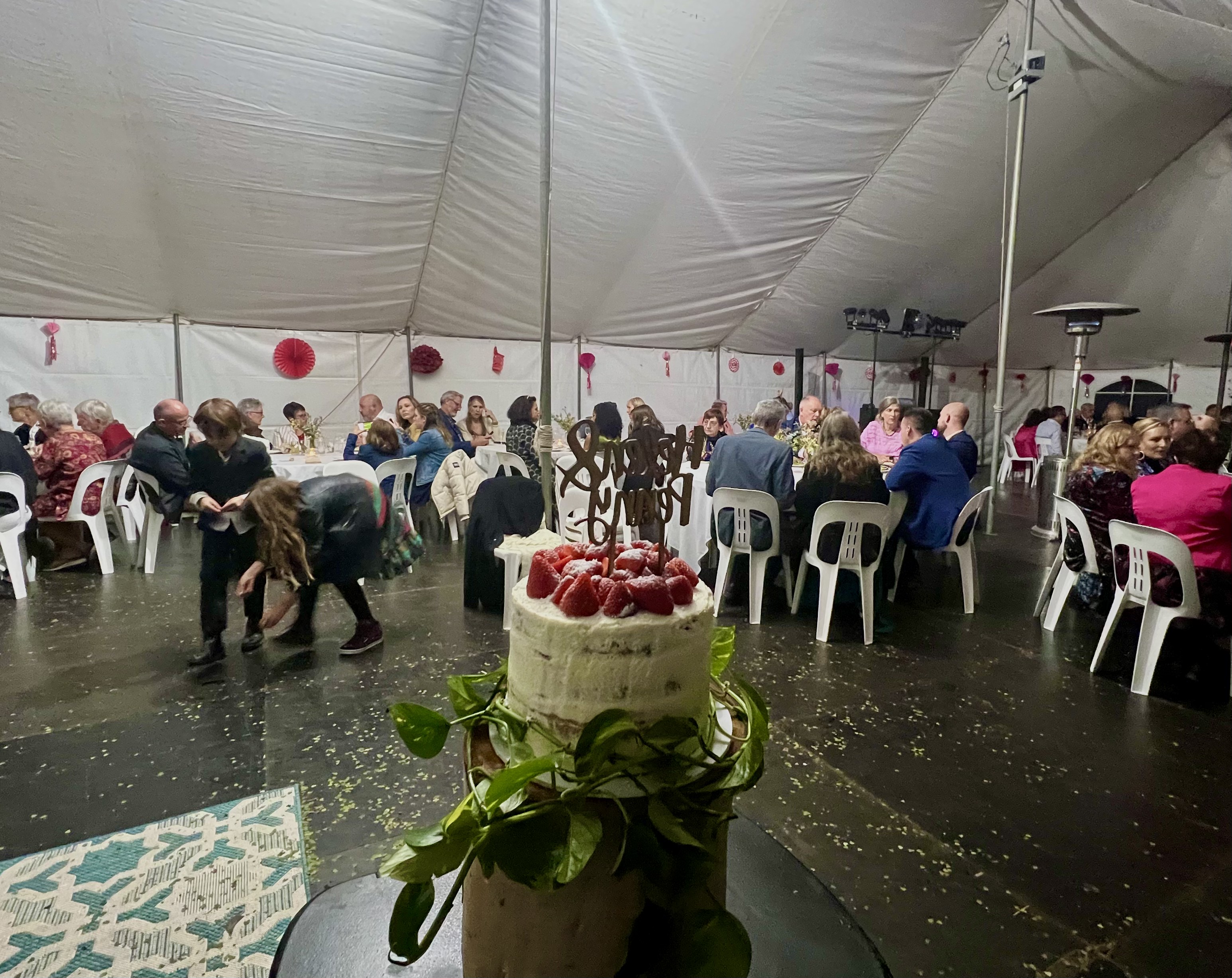 Wedding cake overlooking guests seated for dinner inside the marquee