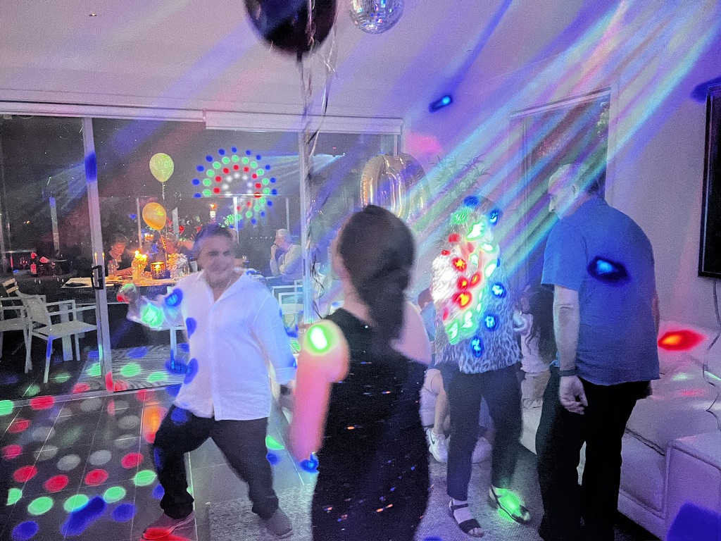 Guests dancing under colourful AMPT party lighting inside the home
