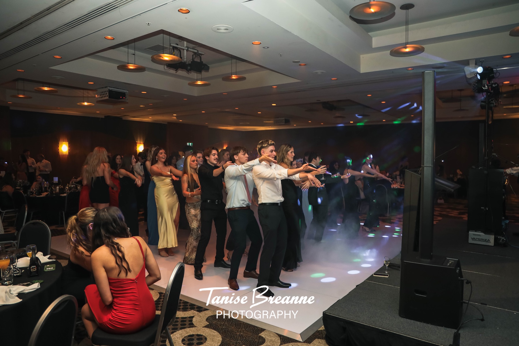 Guests dancing in a line through haze and coloured light