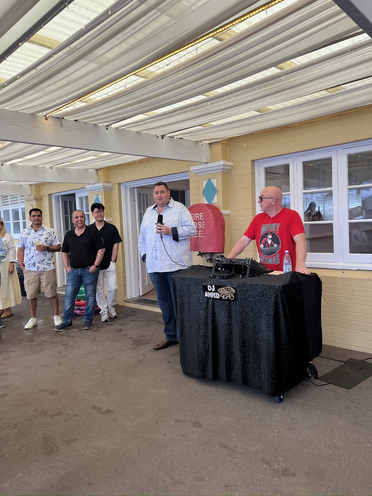 A speaker addressing guests beside AMPT Australia at the DJ booth
