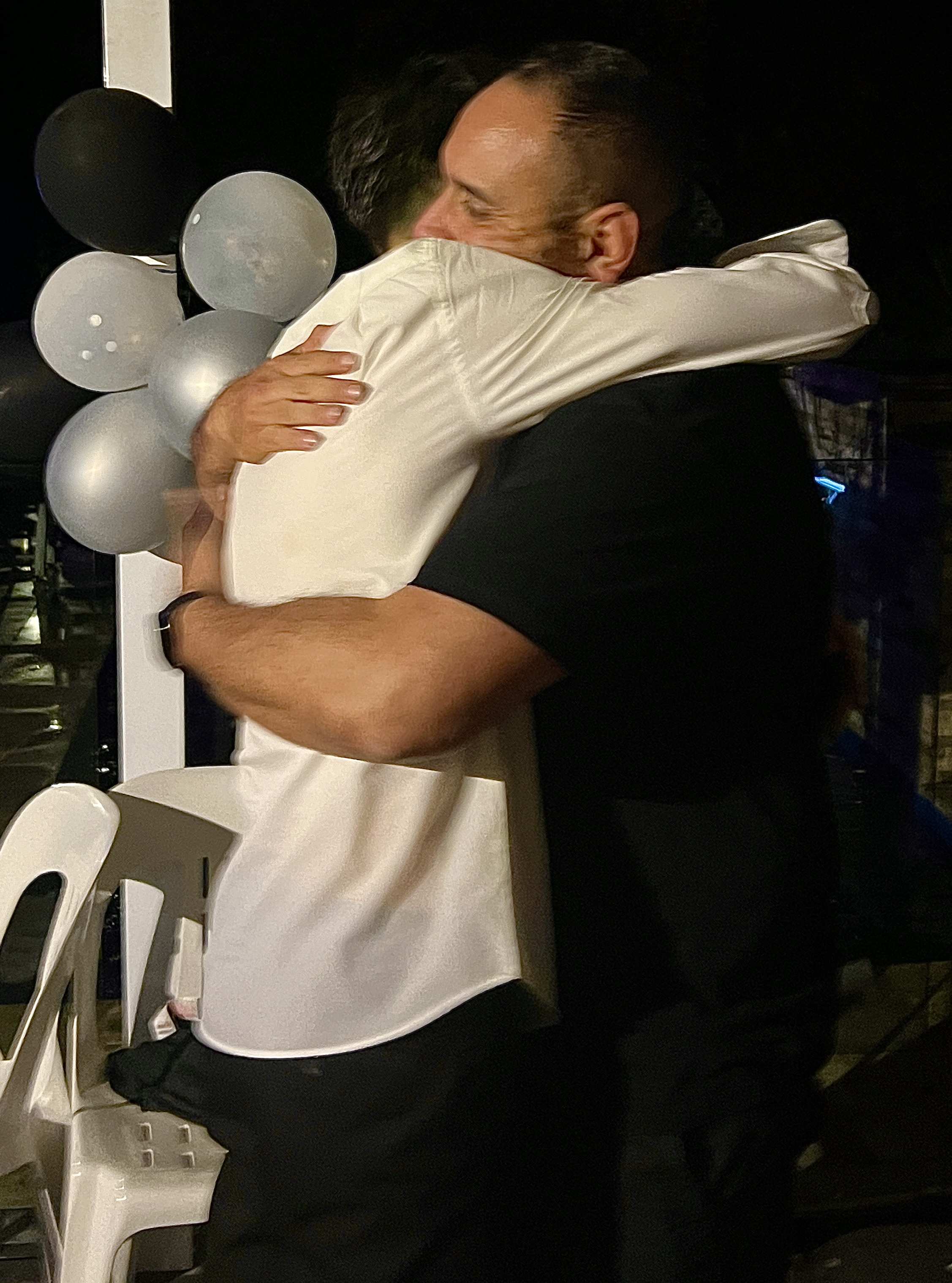 Two people sharing a warm embrace beside party balloons