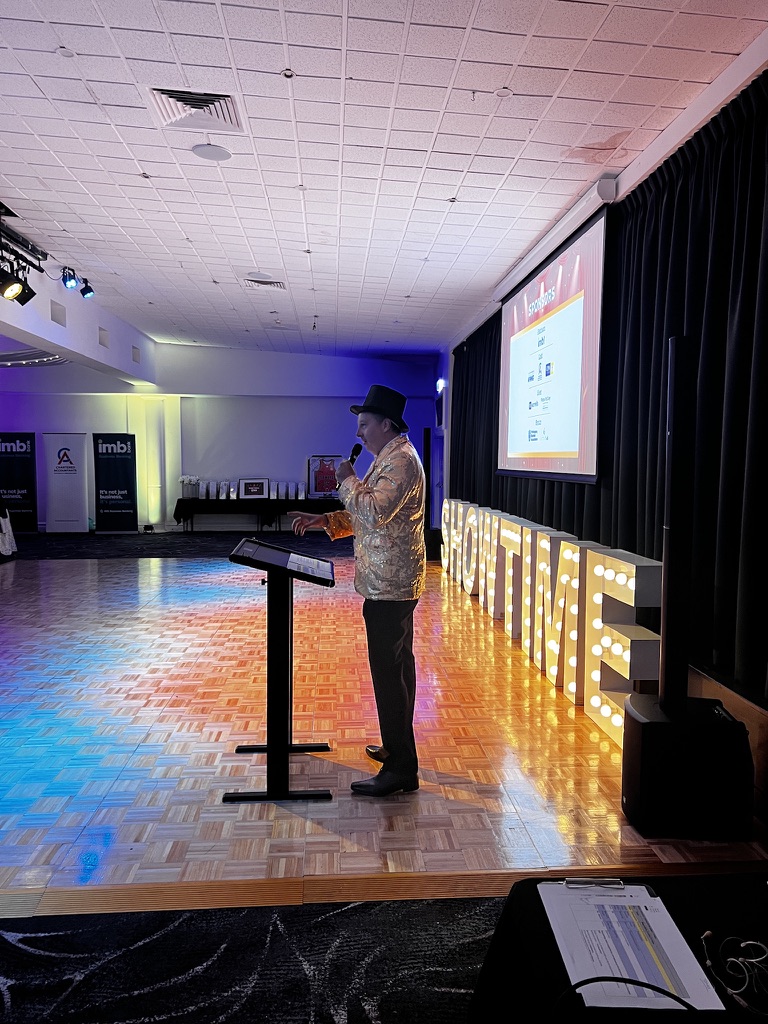 Ryan Cram speaking at the podium in a gold jacket and top hat