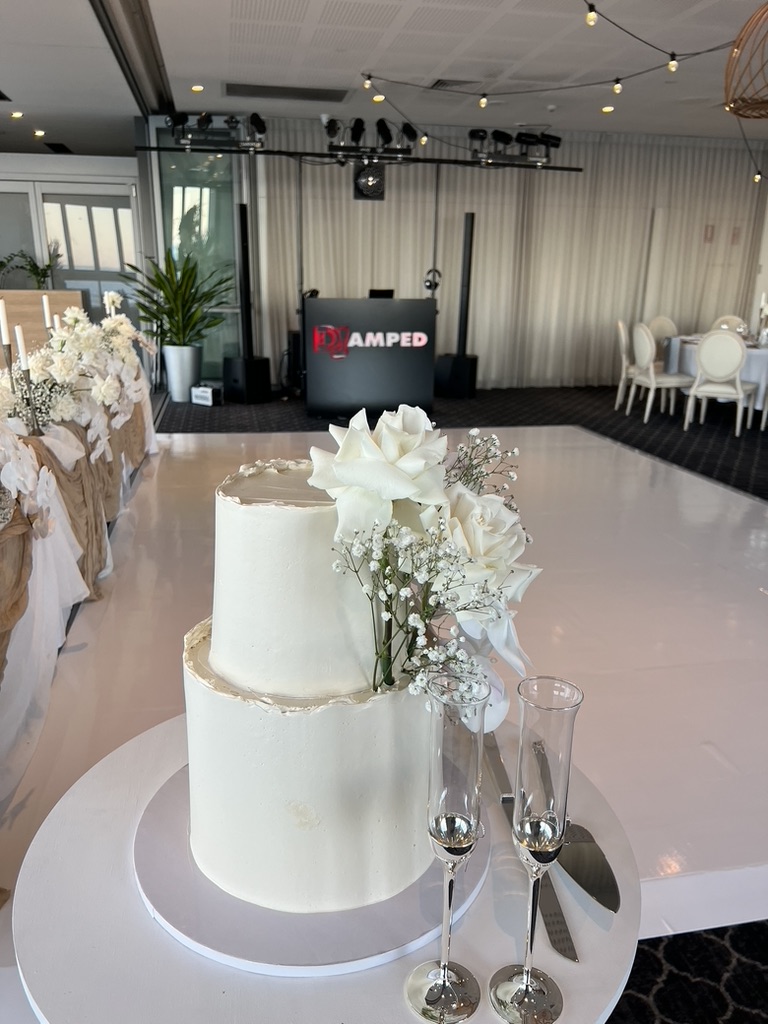 White wedding cake with the AMPT DJ booth behind it